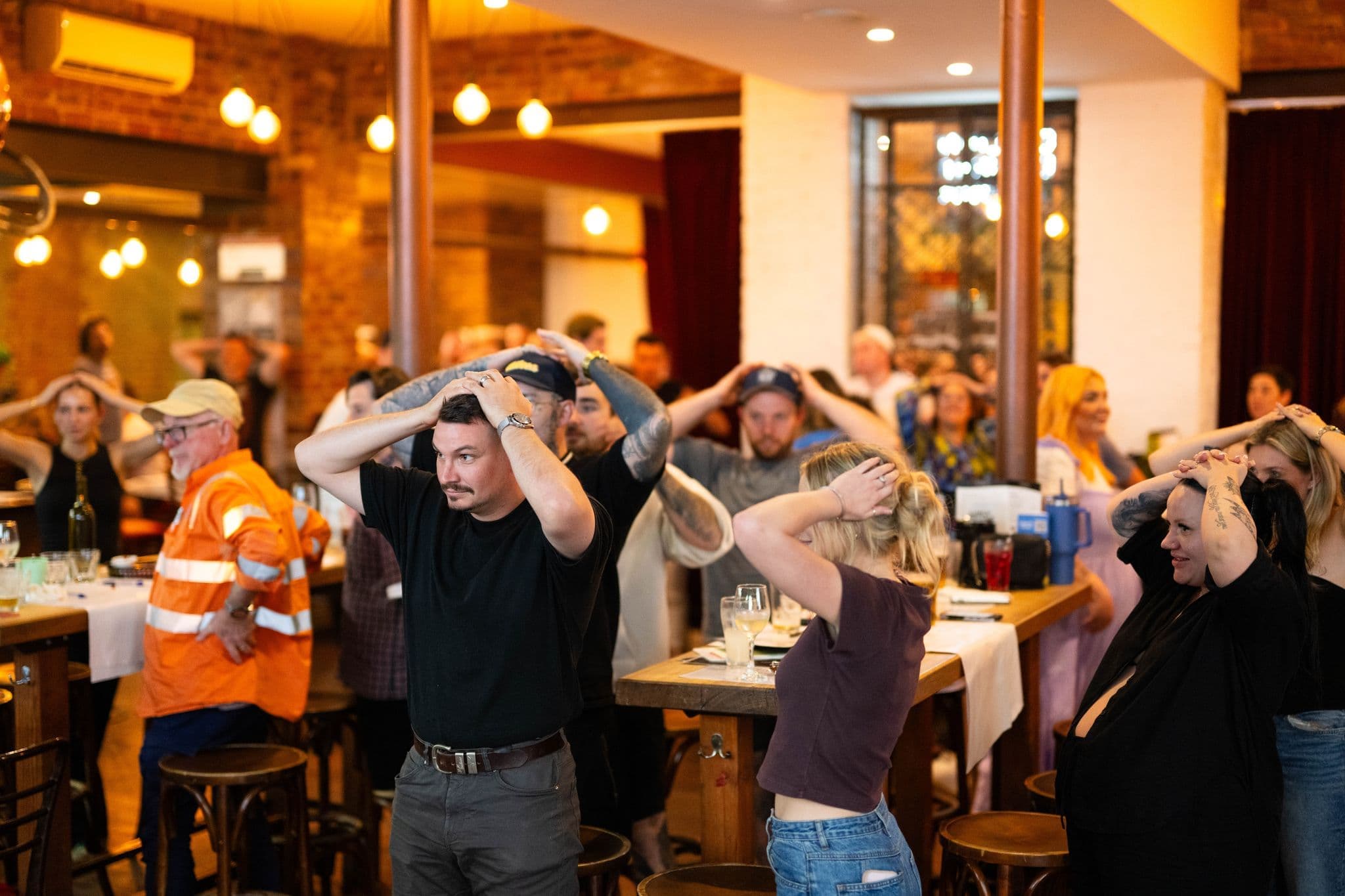 A large crowd of people standing with their hands on their heads, participating in a 'heads or tails' tie-breaker at a Know Brainer Trivia event.