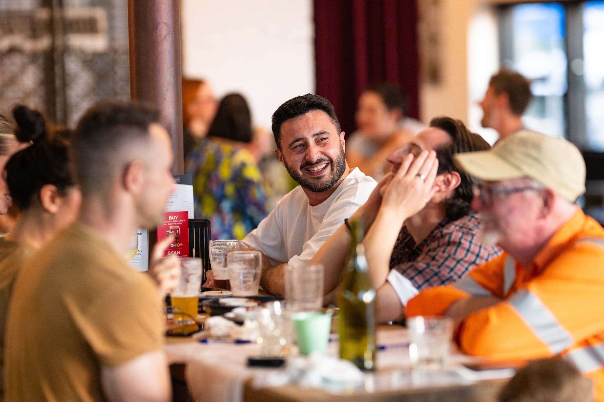 A lively group of friends laughing and enjoying playing a round of Know Brainer Trivia at a pub.